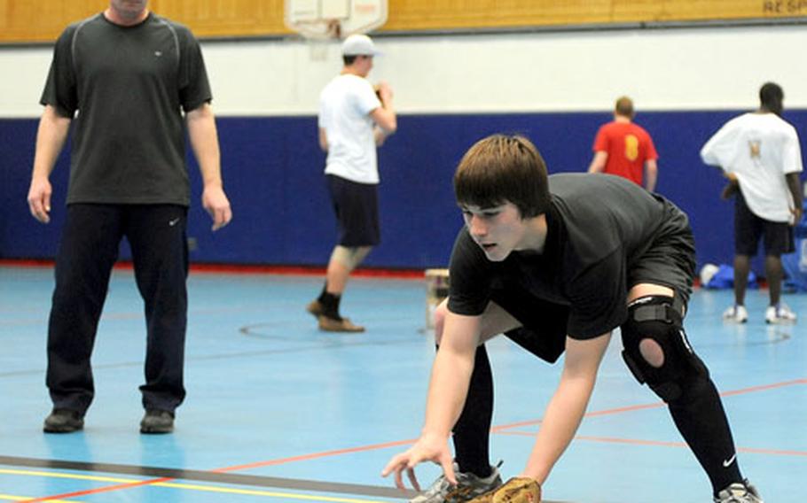 Zack Shull fields a ground ball during practice, as coach Stephen Madl watches in the Ramstein High School gym.