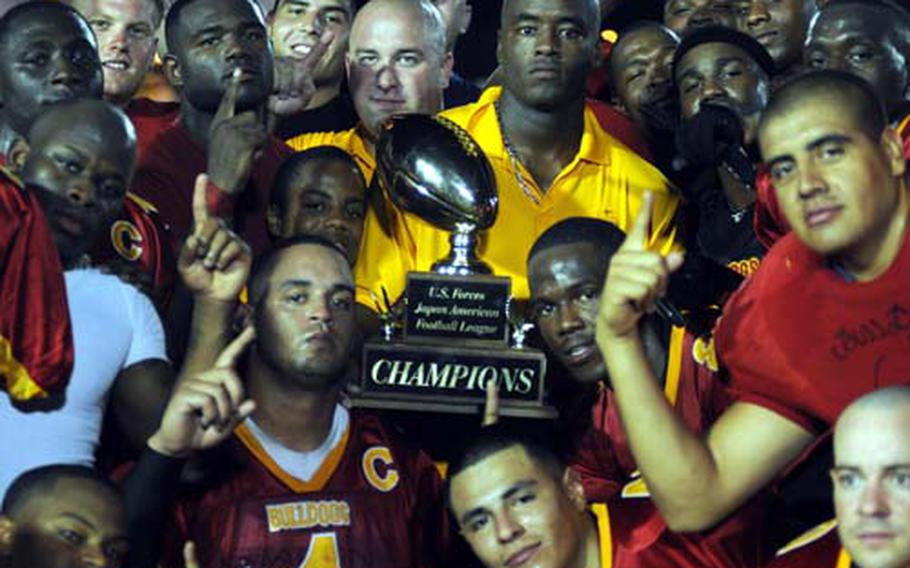 Coach Auburne Edwards, surrounded by his Foster Bulldogs players, holds the U.S. Forces Japan-American Football League&#39;s Torii Bowl trophy following Saturday&#39;s 30-6 win over Yokota.