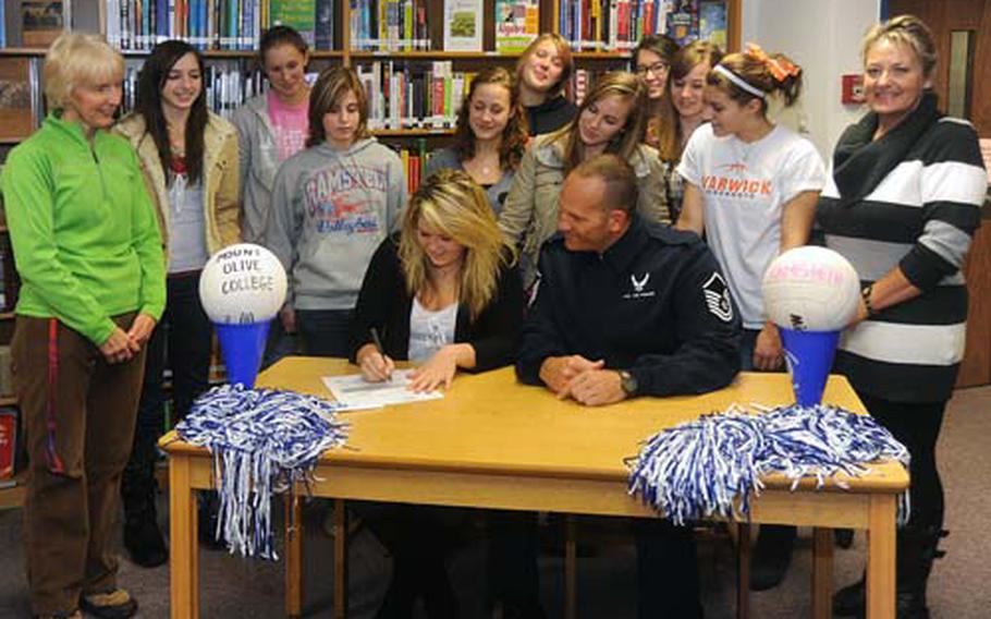 Surrounded by her teammates, parents and coach in the Ramstein High School media room on Monday, Ramstein senior Charnel Austin signs a NCAA Division II national letter of intent with Mount Olive College in North Carolina to play volleyball on scholarship. Sitting at the table with her is her father, Master Sgt. Gary Austin, standing at right is her mother, Gabriele. Charnel’s parents were assistant coaches with the Ramstein varsity team.
