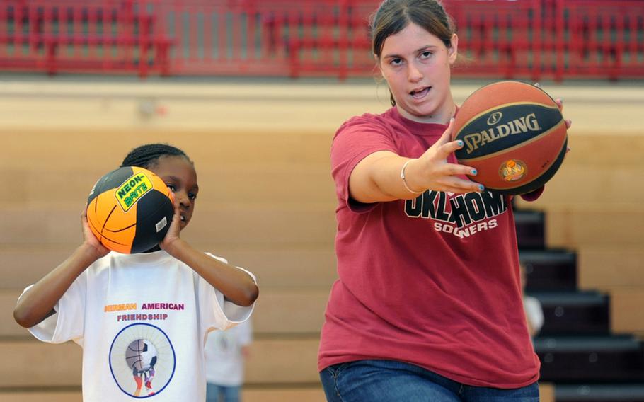 Brittany Hyde, right, shows Taylor McKnight how to throw a basketball at the Mannheim Community?s one-day German-American sports camp at Benjamin Franklin Village and Sullivan Barracks. About 400 youngsters turned out for the camp on Friday that featured basketball, soccer, lacrosse, archery and American football workshops.