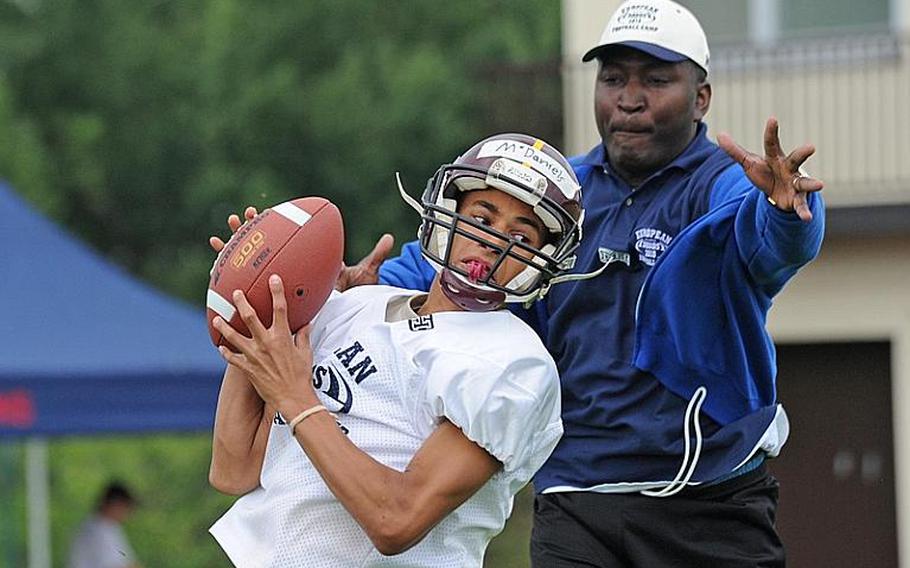 Baumholder's Benjamin McDaniels pulls in a pass in front of Milton Abbott, a coach at Brussels American High School, during a receivers during a drill at the DODDS-Europe football West Camp in Bitburg, Germany, on Wednesday.