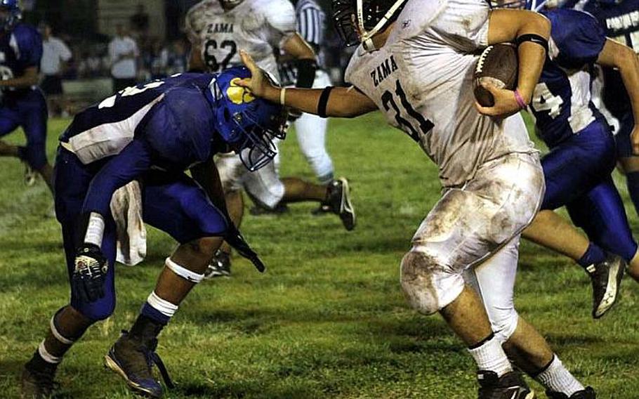 Andre Encarnacion of Zama American stiff-arms Yokota defender Myles Andrews during Friday&#39;s DODDS Japan/Kanto Plain Association of Secondary Schools football game at Bonk Field, Yokota High School, Yokota Air Base, Japan. Yokota won 17-0.