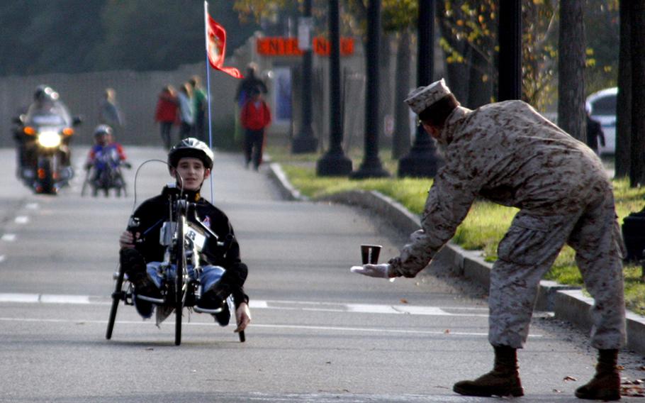 A Marine offers a drink to a hand cycle competitor near the 16-mile mark.