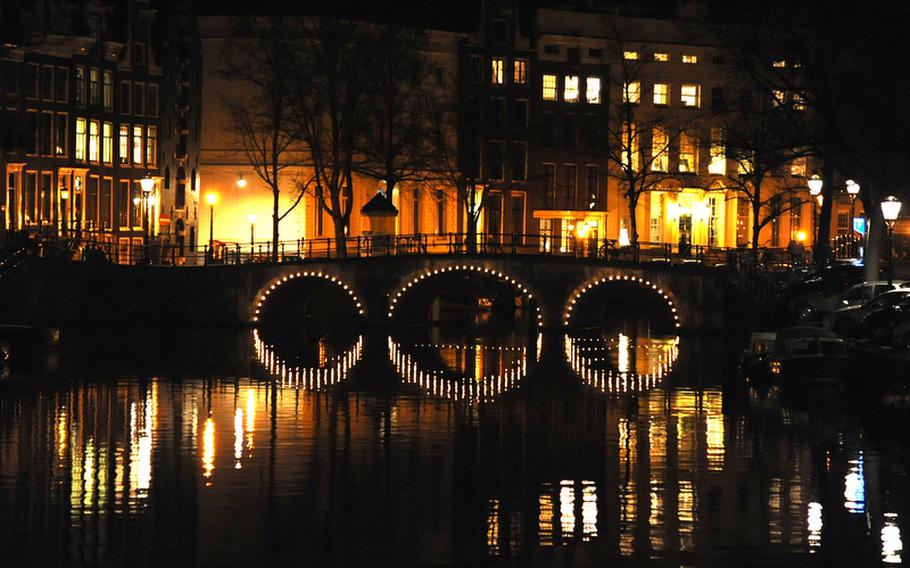 The lights of Amsterdam are reflected in one of the city's many canals.