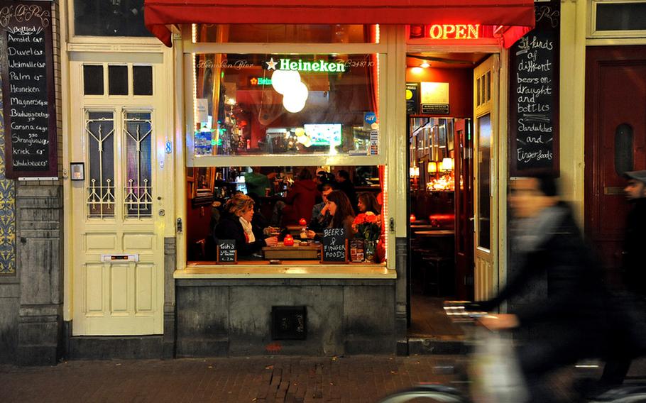 A bicyclist pedals past an Amsterdam pub where patrons enjoy a drink.