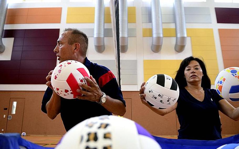 Coach John Kohut, a physical education teacher from Stuttgart, Germany, runs passing and footwork drills while Tina Juliano, a volleyball mom and volunteer from Vicenza, Italy, shags balls at this year's DODDS-Europe volleyball camp at Vilseck High School .