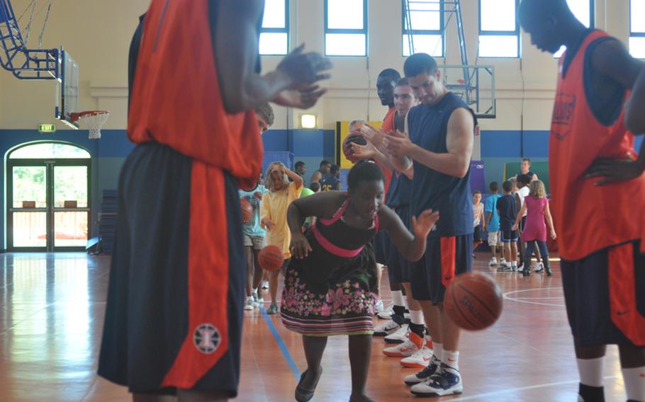 Jataya Mayo, 8, dribbles through a line of clapping Illinois basketball players Wednesday during a clinic on Aviano Air Base put on by players and coaches from Illinois and West Virginia.