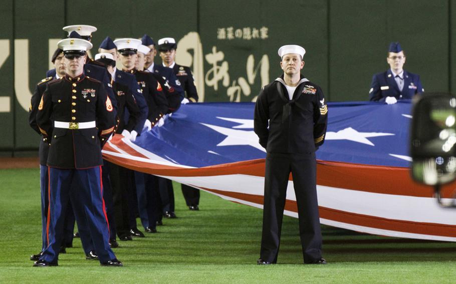 Servicemembers from all branches of the military parade the American flag during the opening ceremony of the American League season opening MLB baseball game between the Seattle Mariners and the Oakland Athletics in Tokyo.