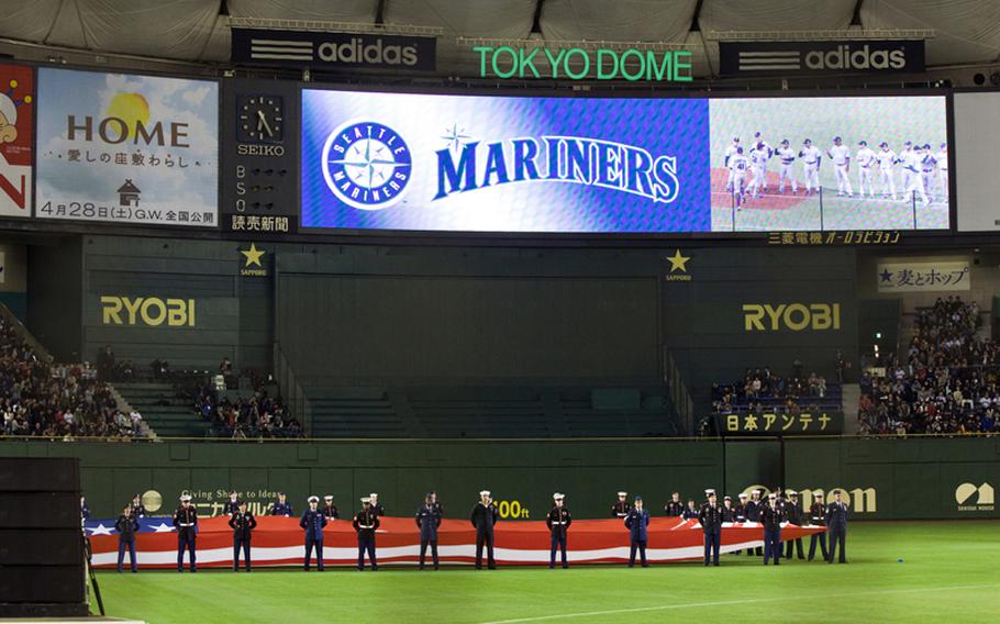 Servicemembers from all branches of the military parade the American flag during the opening ceremony of the American League season opening MLB baseball game between the Seattle Mariners and the Oakland Athletics in Tokyo.