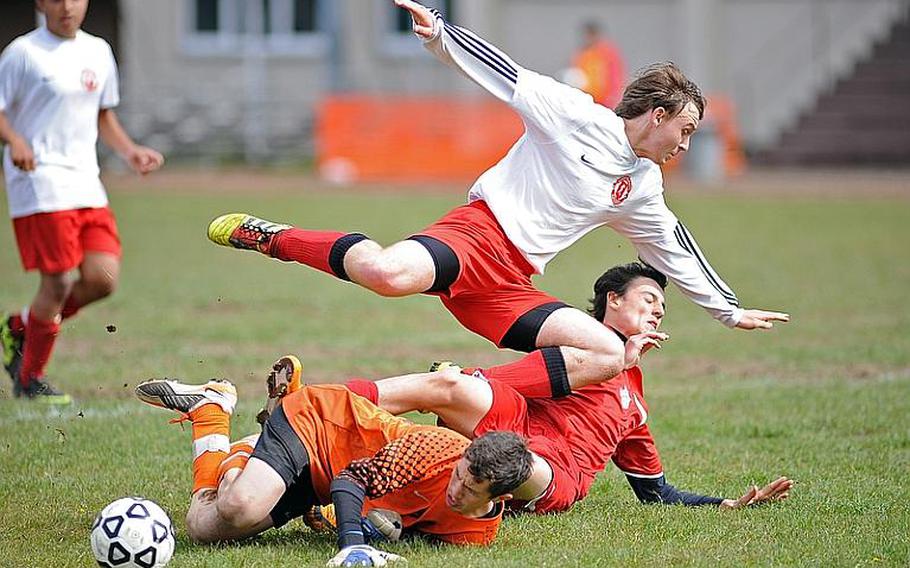 Kaiserslautern keeper Anthony Walker clears the ball out of the danger zone, sending teammate Elijah Crouch, top, and ISB's Alessandro Pryce flying. The two Raiders teams played to a 1-1 tie in Kaiserslautern on Saturday.