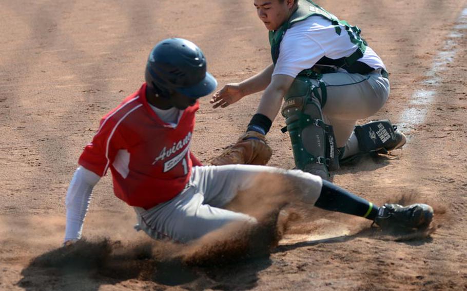 Aviano's Myron McRae slides safely into home plate as Alconbury catcher Isaiah Beltran attempts to tag him during DODDS-Europe baseball action from Ramstein Air Base on Thursday. The Saints defeated the Dragons by a score of 17-1.