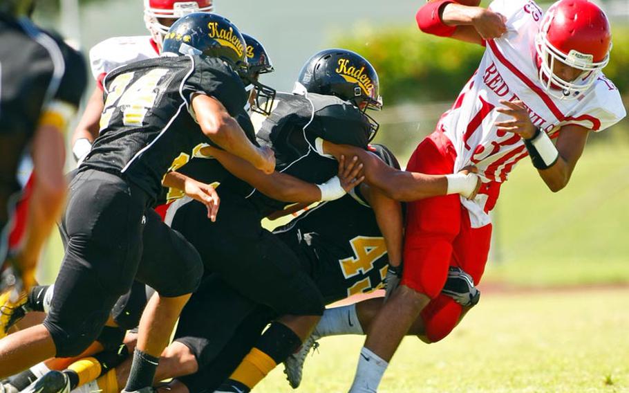 Nile C. Kinnick quarterback Dustin Wilson has the ball knocked out of his hand by Kadena defenders A.J. Sherman, Joseph Hermon and Perry McNeil during Saturday's DODDS Pacific Division I football game at Camp Foster, Okinawa. Kadena routed Kinnick 42-0.