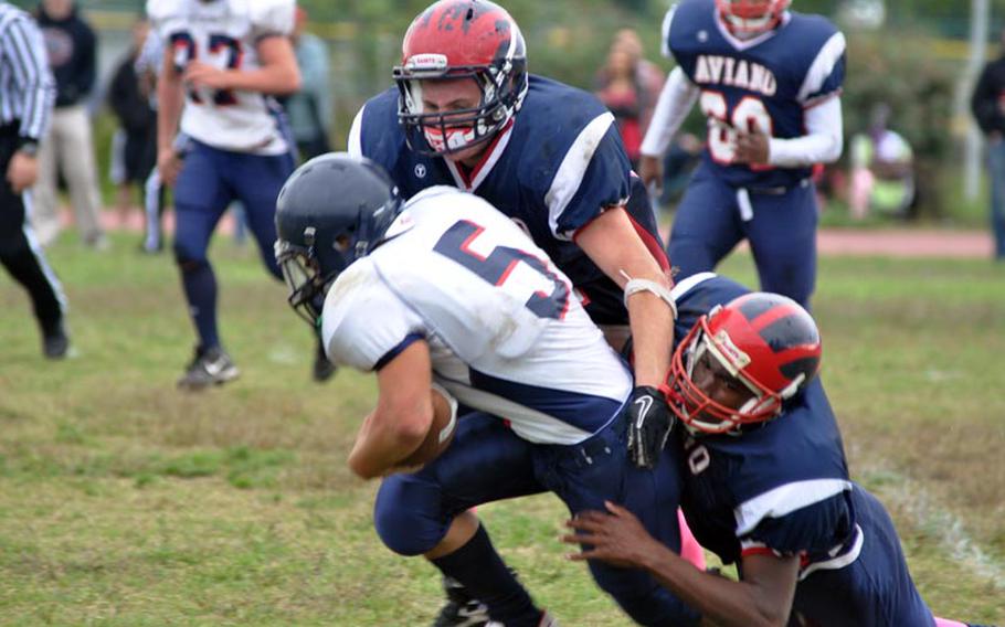 Bitburg's Kenny Love carries two Aviano defenders for a few more yards Saturday in the Barons' 50-6 victory over the Saints. Love had 110 yards rushing in Bitburg's 27th straight victory.