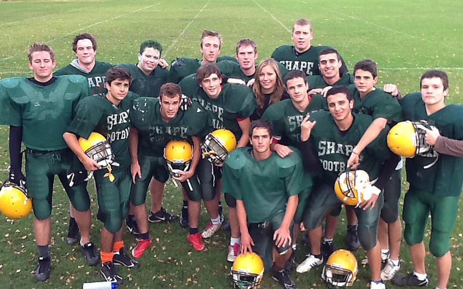 With the exception of placekicker Christoffer Nielson of Ringsted, Denmark, SHAPE's Model U.N. of a football team gets their heads together during a recent practice at Mons, Belgium. Kneeling is Enrique Perales of Ferrol, La Coruna, Spain. In front are, left to right, Lars Bonnevie-Svendsen of Fredrikstad, Norway; Luis Diaz of Cadiz, Spain; Santiago Gamboa of  Madrid; Fernando Royo of Madrid; manager Meghan Fleet, a Canadian; Ignacio Gamboa of Madrid, and Eimad Ismail of Amman, Jordan. Behind them, from left, are Emil Magnussen of Elvrum, Norway; Marek Gernat of Presov, Slovakia; Kristjan Lozar of Ljubljana, Slovenia; Manuel Golmayo of Madrid; Havard Bjornbeth of Maura, Norway; Argios Kollcaku of Tirana, Albania; Luis Palau of  Valencia, Spain, and Antonio Chonevski of Bitola, Macedonia.