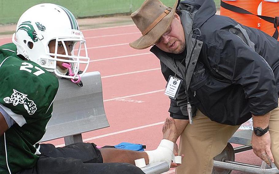 Naples head coach Steve Alstiel takes a break from wrapping Howard Pulley's ankle Saturday to watch a play during the Wildcats' 21-16 victory over SHAPE.