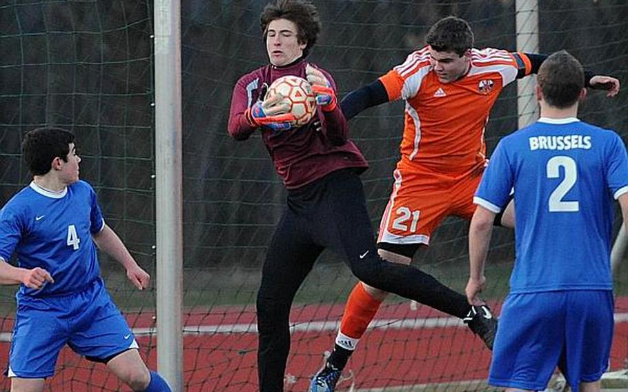 Brussels keeper Danny Helbling pulls in the ball against a flying Luke Narug of AFNORTH in the season opener for both teams at AFNORTH On March 21. The Lions defeated the Brigands in an exciting game 5-4. With a full schedule of high school sports on tap this weekend, AFNORTH will head to Lakenheath, while Brussels will travel to Menwith Hill