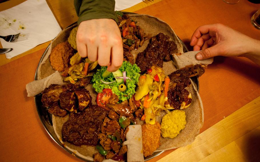 Patrons at the Safari Restaurant in Kaiserslautern, Germany, dig into the Safari, a platter for four featuring a spicy beef stew, cubed lamb with onions and herbs, a succulent chicken stew and lentils and vegetables in Eritrean spices, all served and eaten with “injera,” an East African flatbread.