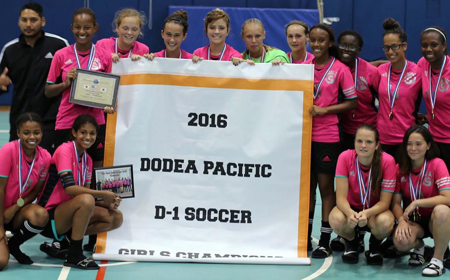 Kubasaki girls soccer players gather around the banner and display their hardware after capturing their third straight Far East Division I Tournament title.