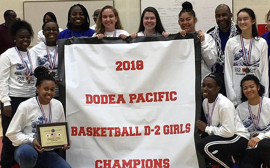 Yokota Panthers girls basketball players gather around the Far East Division II Tournament banner they've won now four straight years.