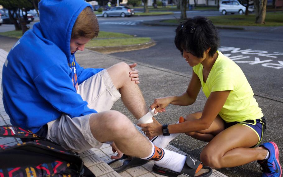 Yokota cross country coach Maggie Chan-Roper tapes junior Daniel Galvin's leg to help manage his shin splint injury during practice Tuesday at Yokota High School. Galvin says he has felt the injury much of the season, but only pulled out of his first race because of it last week.