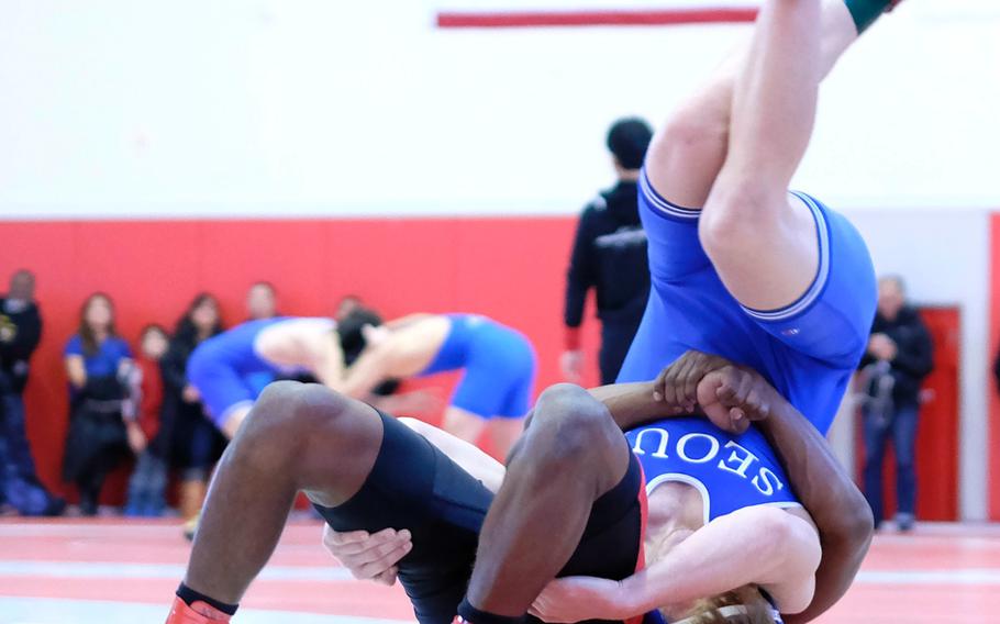 Nile C. Kinnick's Dre Paylor executes a two-hand hip toss on Seoul American's Tristan Johnson at 168 pounds during the Kinnick Invitational "Beast of the Far East" Tournament. Locking hands in an offensive position is legal in international freestyle rules which govern Pacific high school wrestling, but is prohibited in collegiate folkstyle (except for pin combinations).