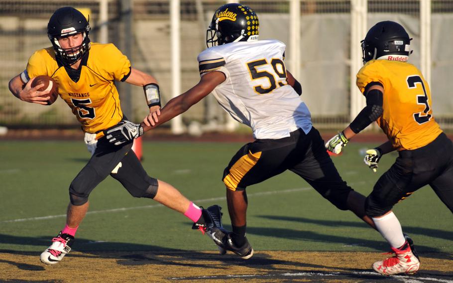 American School In Japan quarterback Jack Ambrosino looks to run out of danger against Kadena defender Tyler Lewis as Mustangs teammate Jo Tsusaka looks to help.