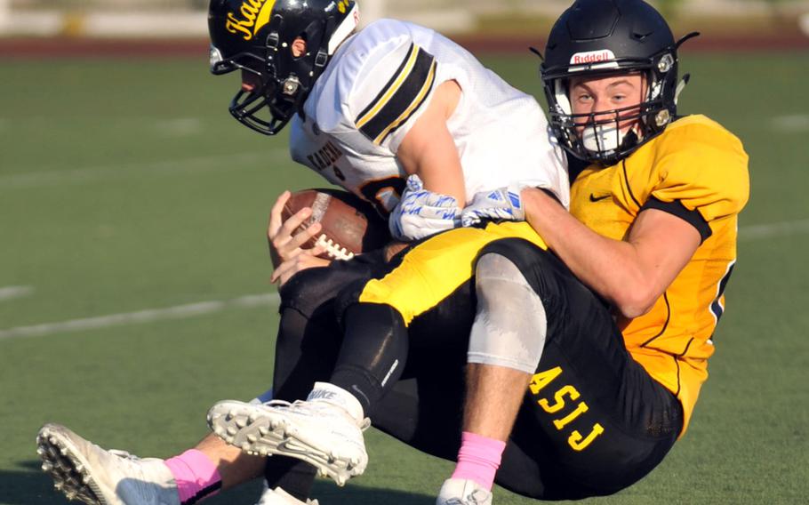 American School In Japan defender Mike Taylor wrestles Kadena quarterback Cody Sego to the ground.