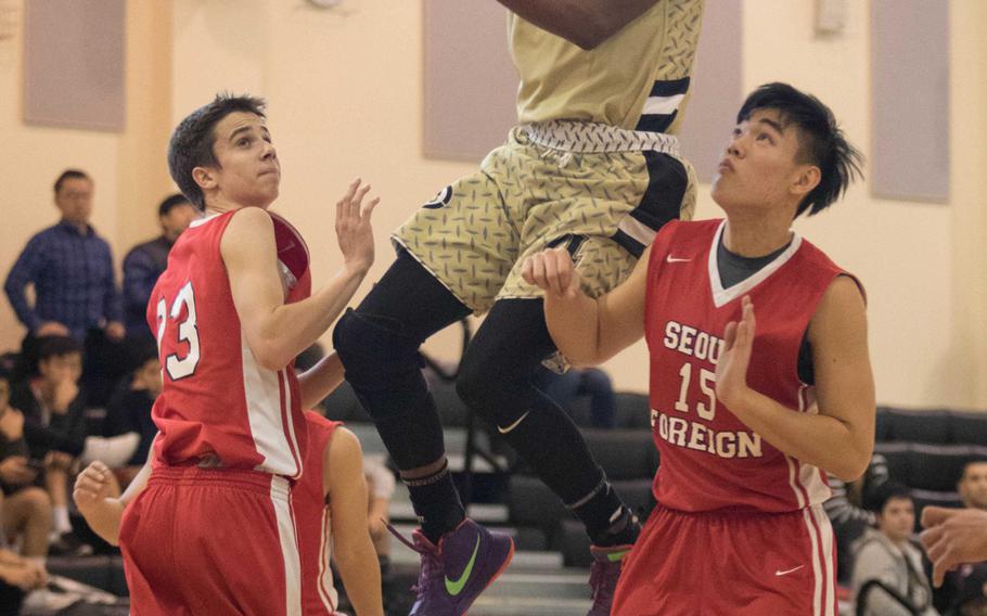 Humphreys' Nate Hellams goes airbornefor the shot between Seoul Foreign's Nick Larsen and Daniel Bang during Saturday's boys basketball game, won by the Blackhawks 54-51.