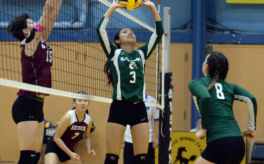 Kubasaki setter Mimi Larry readies a set for teammate Abigail Robinson as Seisen's Amanda Wood jumps to block at the net during Saturday's American School In Japan-YUJO III girls volleyball tournament. The Phoenix swept the Dragons in straight sets.