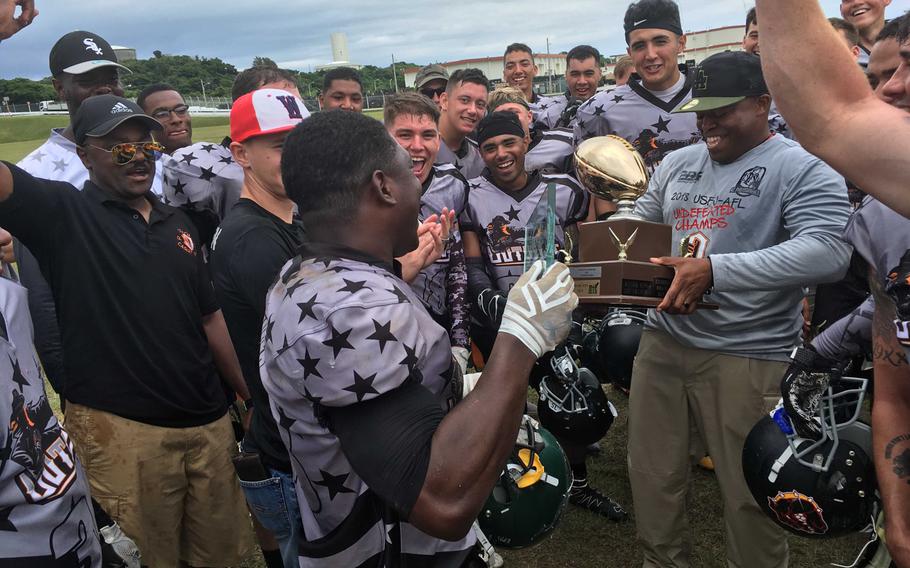 Benjamin Fuller, center, holds the Joe Howell MVP Award and Hansen Outlaws coach Dean McCown Sr. the Torii Bowl championship trophy as teammates surround and celebrate following the Outlaws' 40-22 win Saturday over Ryukyu University in the U.S. Forces Japan-American Football League title game.