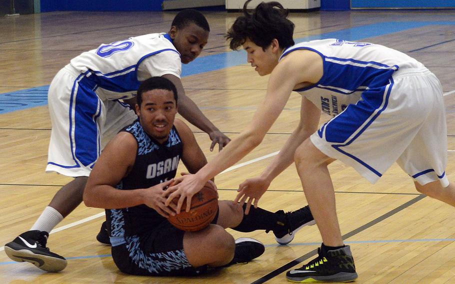 Osan's Jaden Wright has the ball tied up by Seoul American's Bevani Lauzon and Elijah Houghton during Wednesday's boys basketball game. The Cougars won 56-30.