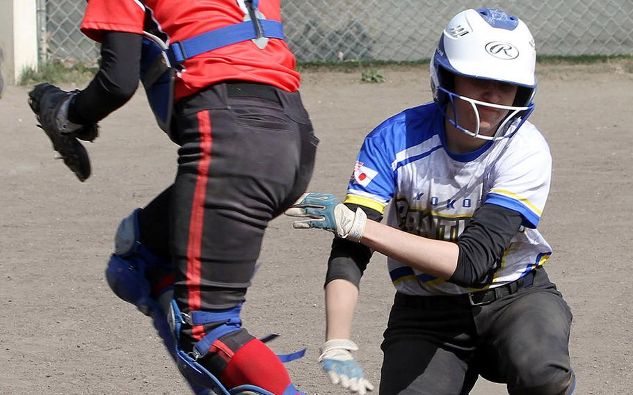 Yokota's Adrianna Diaz slides in at home as Nile C. Kinnick catcher Faith Sells turns to chase an overthrown ball during Saturday's DODEA-Japan softball tournament final. The Panthers won 11-9.