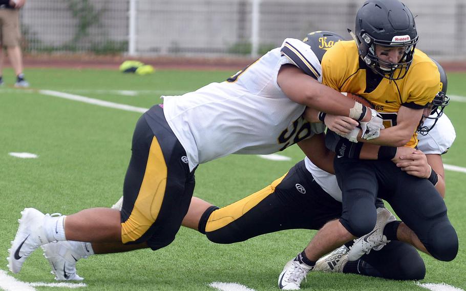 Kadena defenders Jace Salas and Dean Owen wrestle American School In Japan running back Allen Edmonds to the turf.