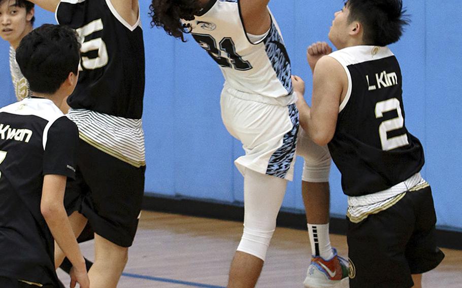 Osan's Israel Rouse shoots between two Taejon Christian defenders during Saturday's Korea Blue boys basketball game. The Cougars won their first game in six tries 67-44 over the Dragons.