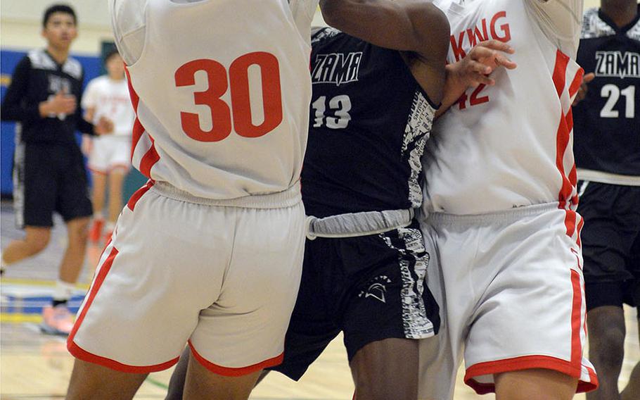 Zama's Chandler Platt tries to navigate between E.J. King's Jalen Nall and Tsuyoshi Kemp during Friday's DODEA-Japan boys semifinal, won by the Trojans 62-53.