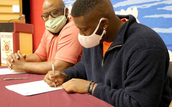Seated beside his father Linnon, Matthew C. Perry senior Marshall China, three-time Far East heavyweight wrestling champion, signs a National Letter of Intent to compete at Division I Campbell.