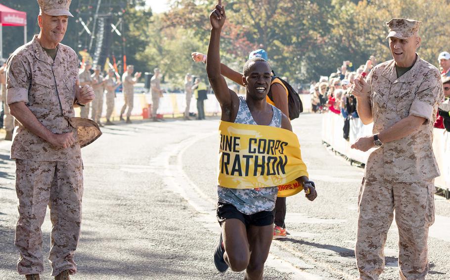 Army Spc. Samuel Kosgei crosses the finish line as the winner of the men's division of the 39th Annual Marine Corps Marathon, Oct. 26, 2014. Holding the tape were Marine Corps Commandant Gen. Joseph F. Dunford Jr., left, and Assistant Commandant Gen. John M. Paxton Jr.