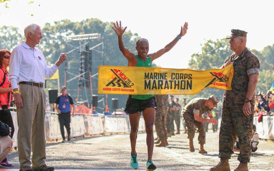 Desta Beriso Morkama, the first male finisher of the 42nd Marine Corps Marathon, crosses the finish line as Marine Commandant Gen. Robert Neller holds the finish line banner.