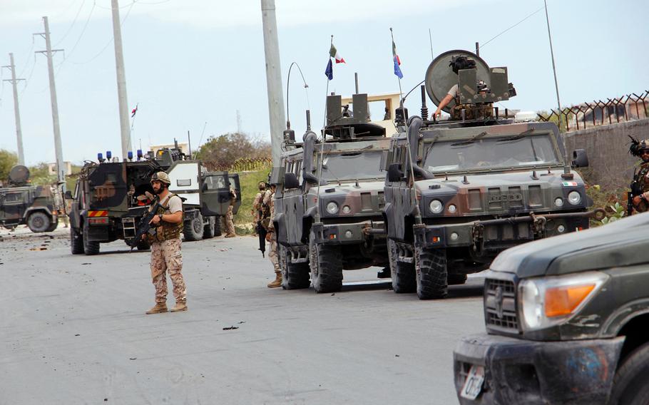 A member of the Italian military stands next to a damaged armored personnel carrier after an attack on a European Union military convoy in the capital Mogadishu, Somalia Monday, Sept. 30, 2019. 