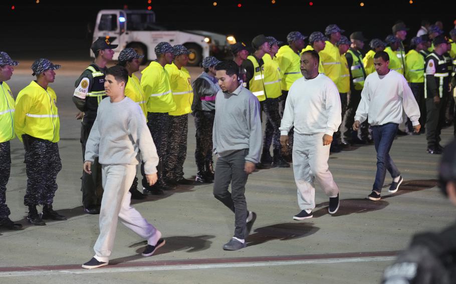 Deported migrants walking in a line at an airstrip.