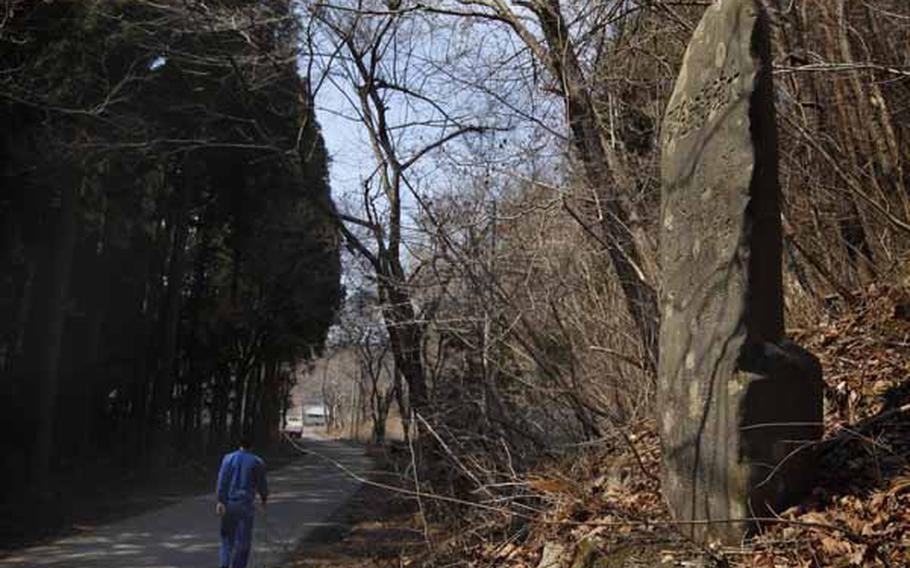 In this March 31, 2011 photo, a tsunami survivor walks past a centuries-old tablet that warns of danger of tsunamis in the hamlet of Aneyoshi, Iwate Prefecture, northern Japan. Hundreds of such markers dot the coastline, some more than 600 years old. Collectively they form a crude warning system for Japan, whose long coasts along major fault lines have made it a repeated target of earthquakes and tsunamis over the centuries. 