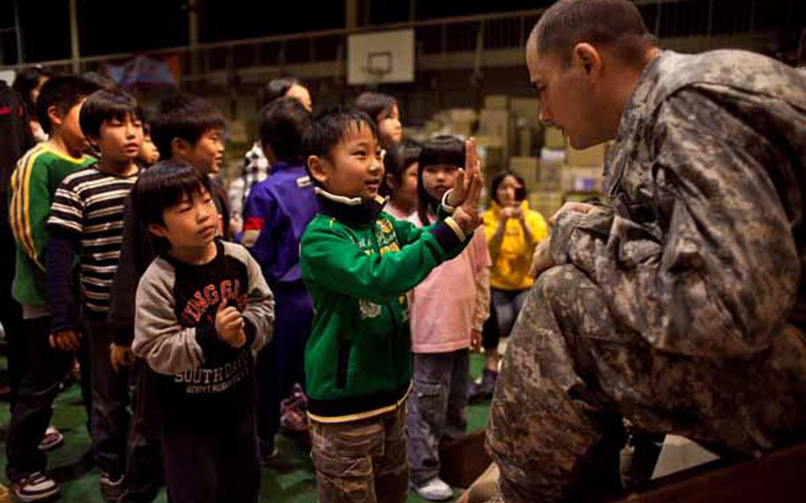 Staff Sgt. Jeff Kurka, 35, a trombone player for the Camp Zama Army Band, asks a boy at the Rokugo Middle School shelter in Sendai City how old he is. The band played a concert for the residents of the shelter and brought gifts for the children donated by the Camp Zama Boy Scouts and Girl Scouts associations.