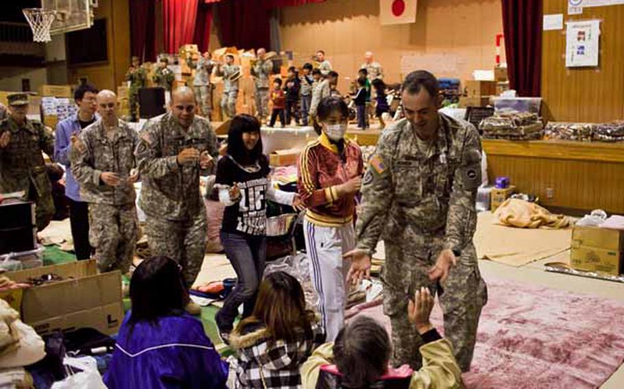 Members of the Camp Zama Army Band play and dance with children on stage while other members lead a conga line of soldiers and displaced residents around the Rokugo Middle School shelter in Sendai City, Japan.