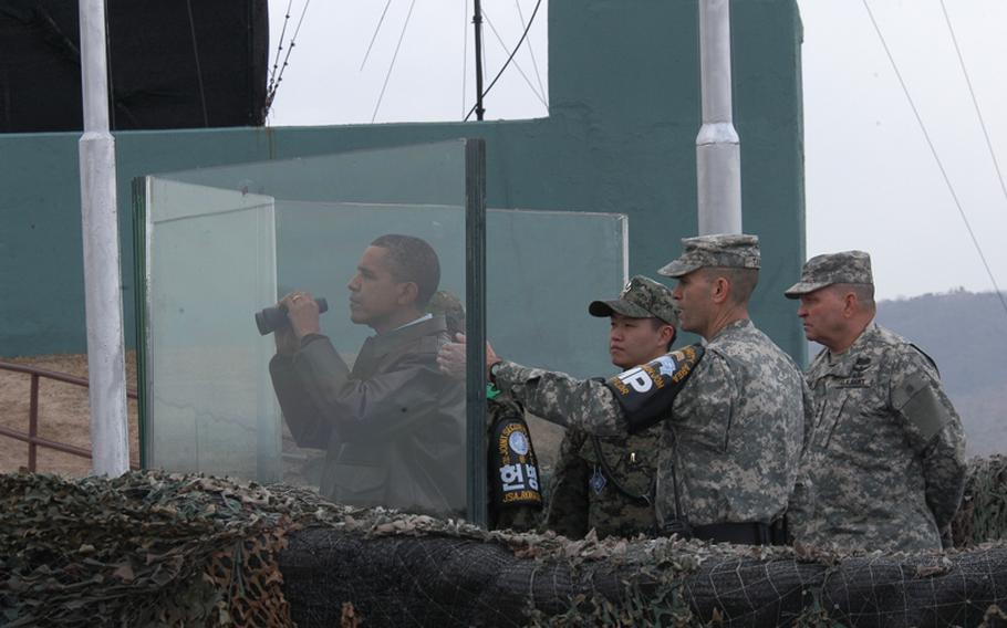 President Barack Obama looks over binoculars through protective glass at North Korea on March 25, 2012, from an observation post 25 yards from the Military Demarcation Line that divides the two Kores. Lt. Col. Ed Taylor, commander of the United Nations Command Security Battalion - Joint Security Area, center describes some of the landmarks of the Demilitarized Zone to Obama as U.S. Forces commander Gen. James Thurman, right, looks on.     