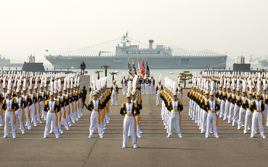 Midshipmen at the Republic of Korea Naval Academy stand in formation, with ROK Navy ships and submarines in the background and U.S. Navy Rear Adm. Bill McQuilkin in attendance.
