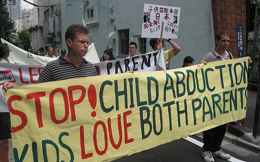 Two Canadian men, who asked not to be identified, hold a sign during a demonstration in August 2011 in Tokyo advocating dual custody rights for divorced parents in Japan. Japan’s legislature passed a bill May 20, 2013,  authorizing the government to sign an international treaty to prevent international child abductions.