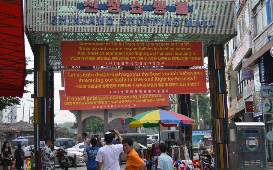 Passers-by take photos of banners at the Shinjang Shopping Mall that protest off-limits orders for Americans on several bars in the entertainment district outside Osan Air Base, South Korea, on Thursday, June 13, 2013.