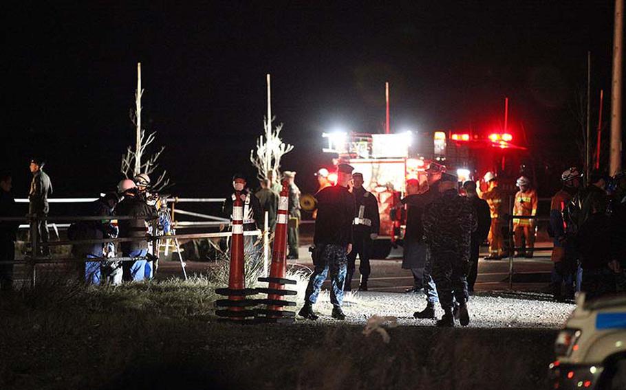 Japanese workers and U.S. Navy personnel survey the scene Monday, Dec. 16, 2013, where a U.S. Navy Knighthawk helicopter crash-landed in an empty area of reclaimed land about 10 miles southwest of Yokosuka Naval Base.