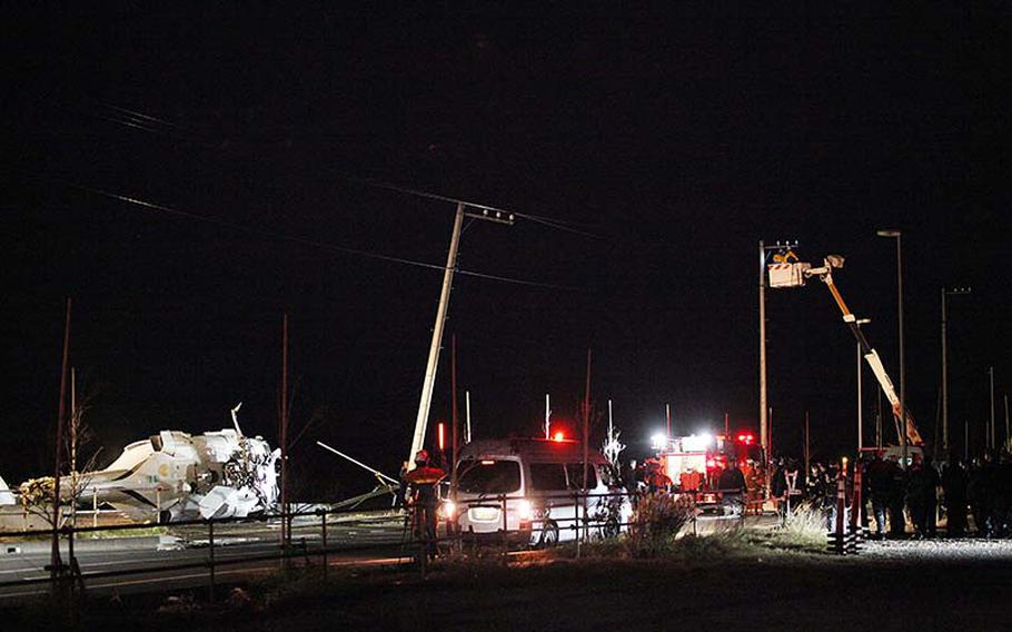 Japanese workers and U.S. Navy personnel survey the scene Monday, Dec. 16, 2013, where a U.S. Navy Knighthawk helicopter crash-landed in an empty area of reclaimed land about 10 miles southwest of Yokosuka Naval Base.