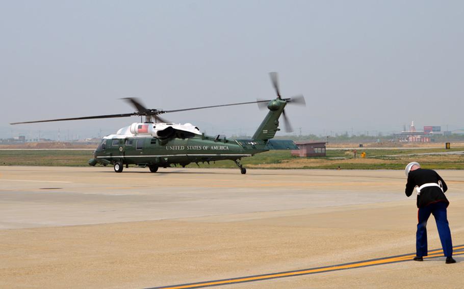 A member of the U.S. Marine Corps Presidential Security Forces holds his dress hat as President Barack Obama departs in Marine One from Osan Air Base, South Korea, on Friday, April 25, 2014.